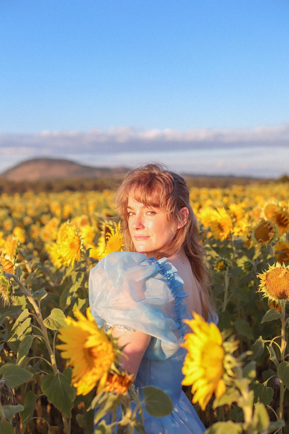 A woman in a blue selkie dress stands in a sunflower field